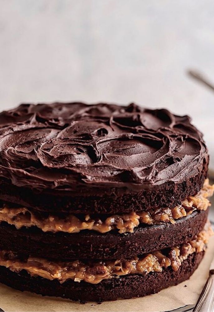 Close view of a tall dark chocolate layer cake with thick swirled ganache on top and toasted walnut filling visible between moist cocoa layers