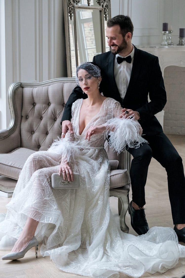 Positive Newlywed Couple In Fancy Gowns Sitting On Comfy Sofa