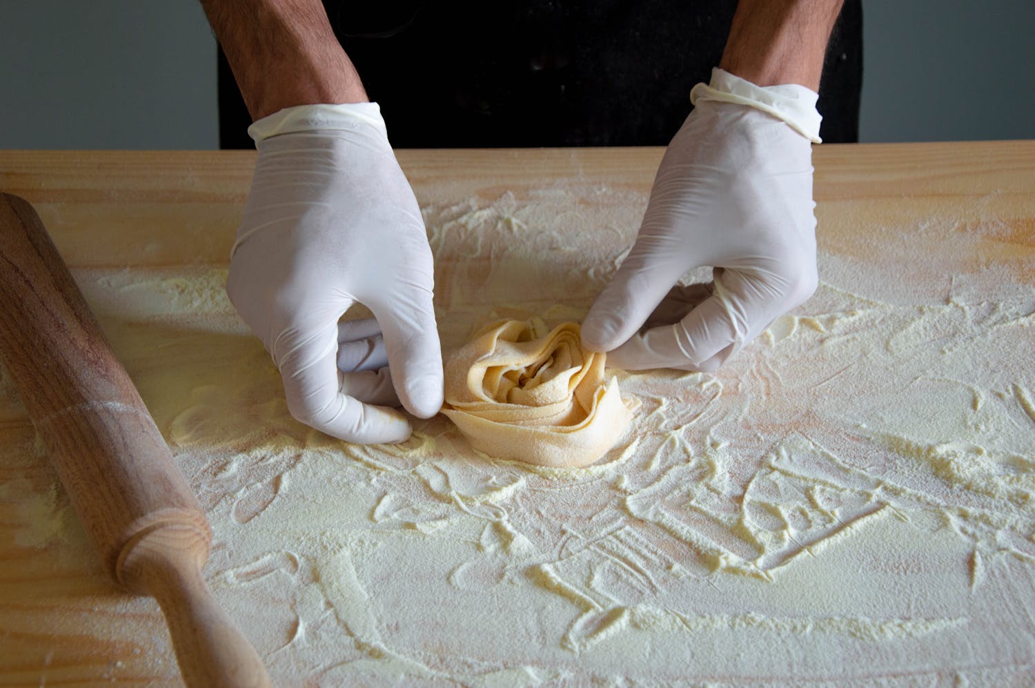 Hands wearing gloves making homemade pasta on wooden surface
