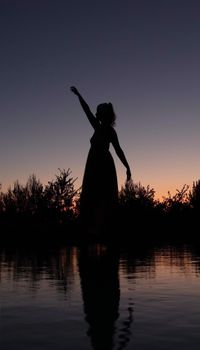 Artistic silhouette of a woman at twilight reflecting on water.