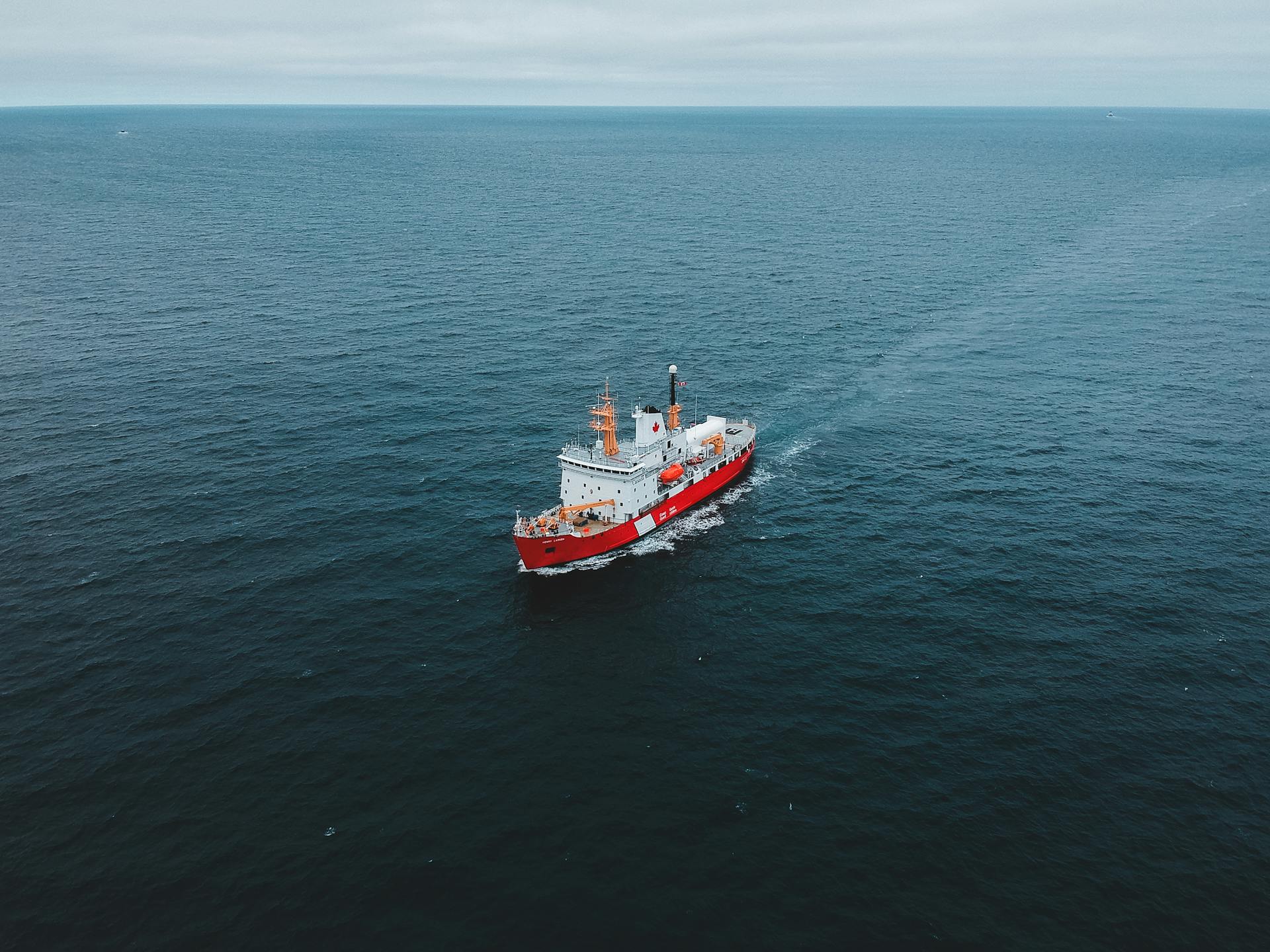 Aerial view of a prominent red ship navigating the expansive blue ocean, showcasing maritime transport.