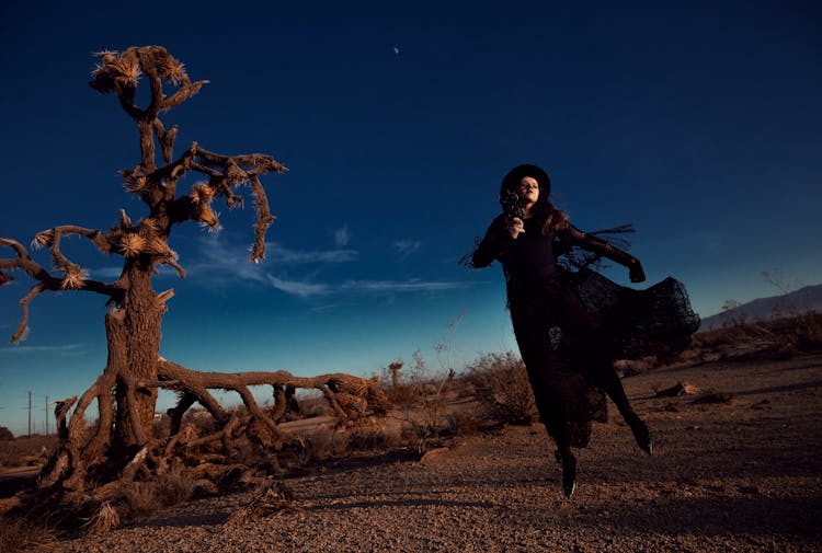 Jump Shot Of A Woman In A Steampunk Outfit Beside A Joshua Tree