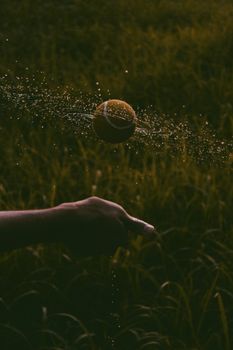 A tennis ball spinning mid-air with splashing water droplets creating a dramatic effect against a blurred background.