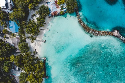 Free Aerial top view of turquoise seawater washing sandy shore with exotic greenery and small coastal settlement Stock Photo