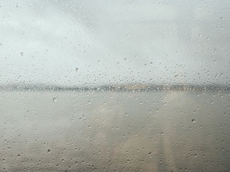Blurred window glass covered with rain drops and landscape of gloomy sea under clouds