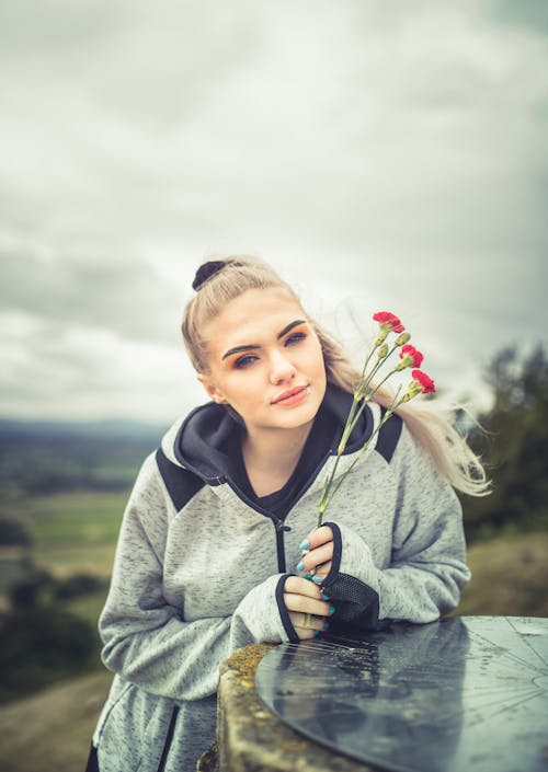 Photo of Woman in Gray Hoodie While Holding Red Flowers