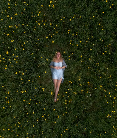 Free Aerial view of a woman lounging in a green field with yellow blooms, exuding peace and tranquility. Stock Photo