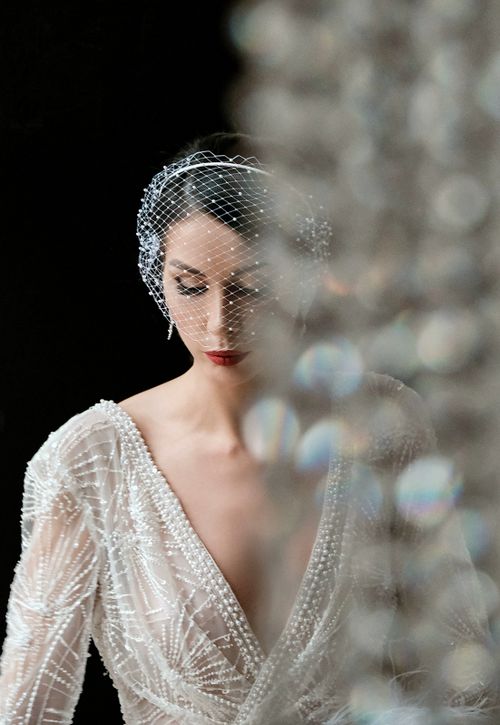 Free Through decorative glass calm gorgeous bride in chic white dress standing against black background in studio and looking down Stock Photo