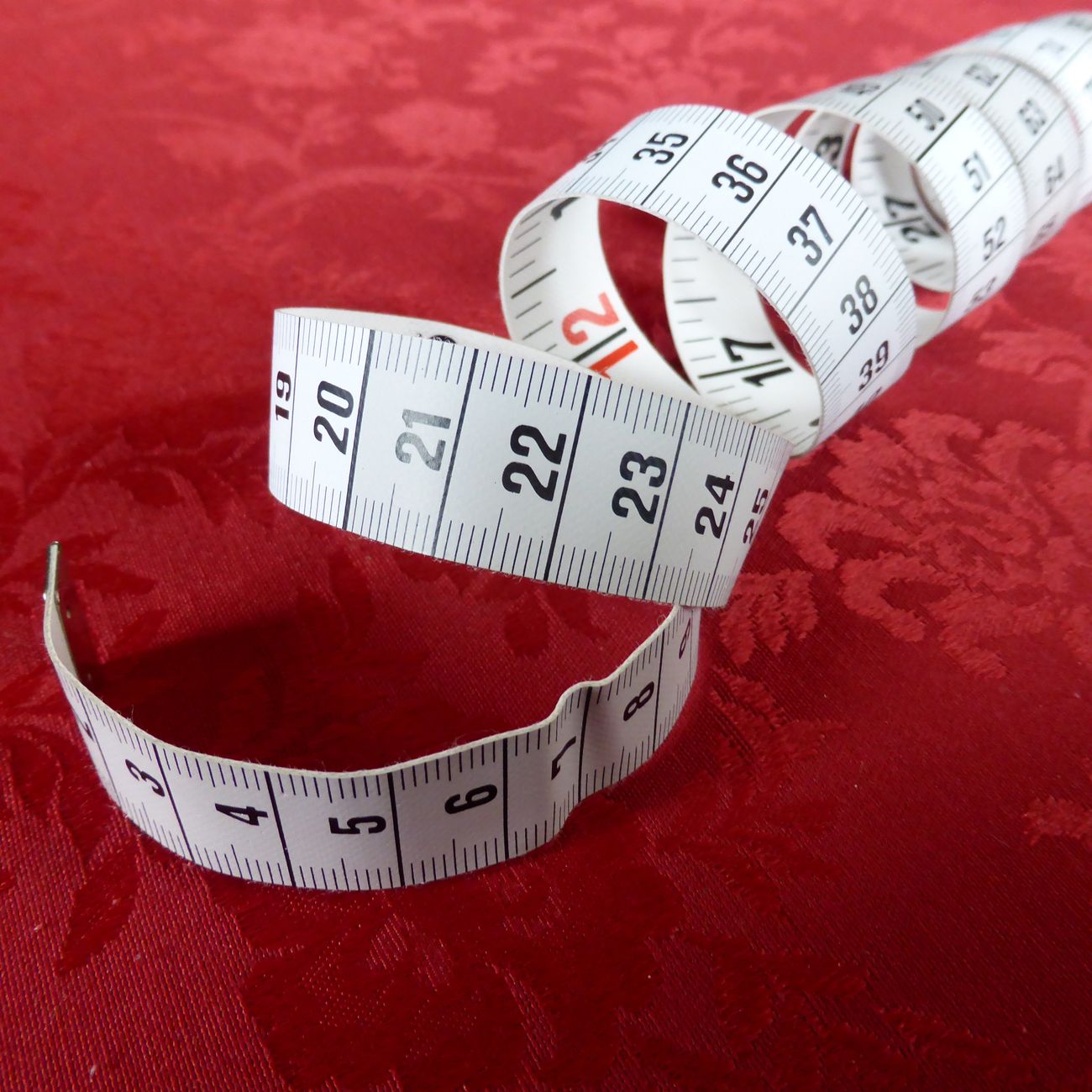 White measuring tape coiled on red patterned fabric, close-up view.