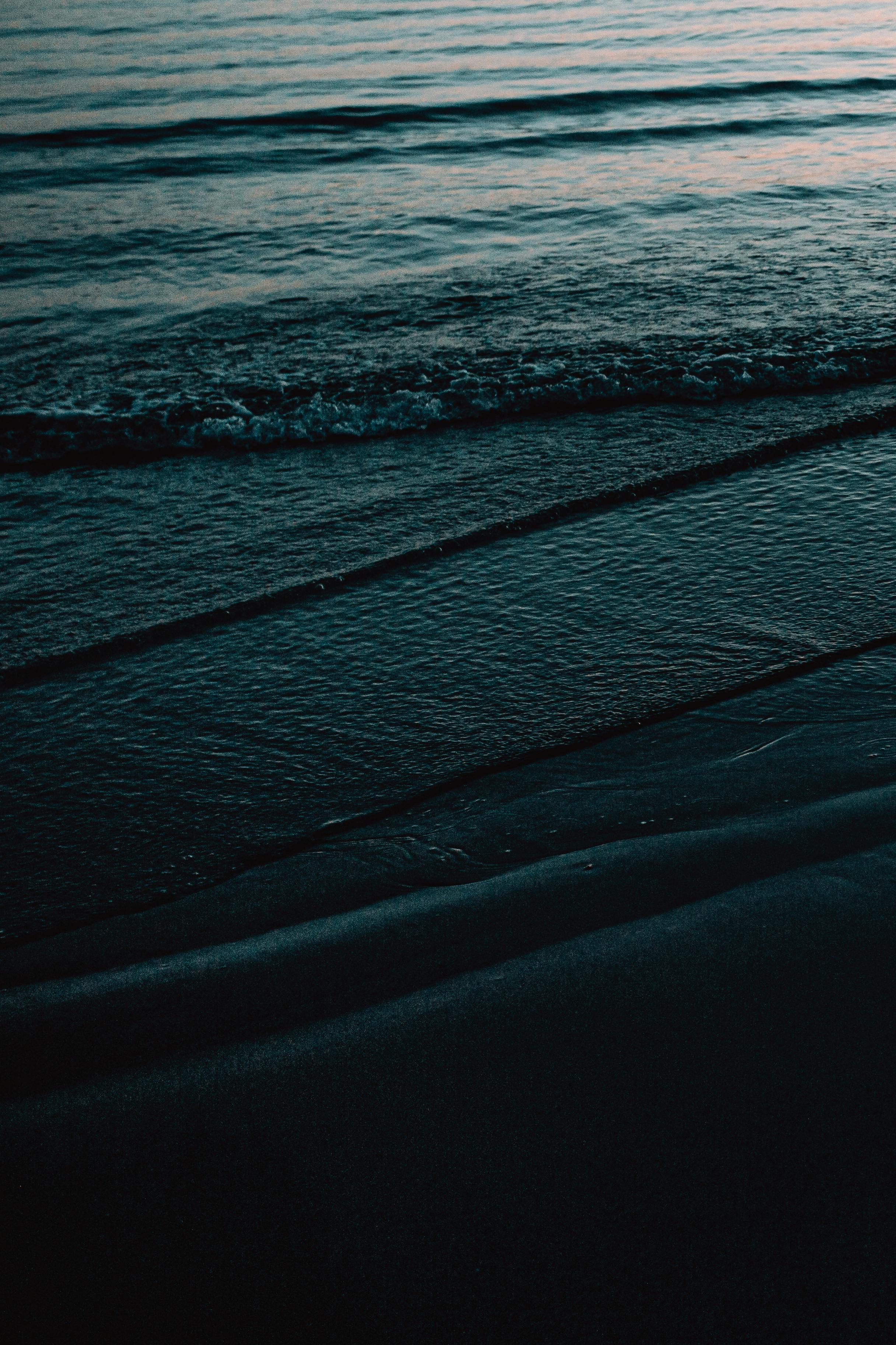 A serene view of ocean waves gently reaching a dark sandy beach at dusk, capturing nature's tranquility.