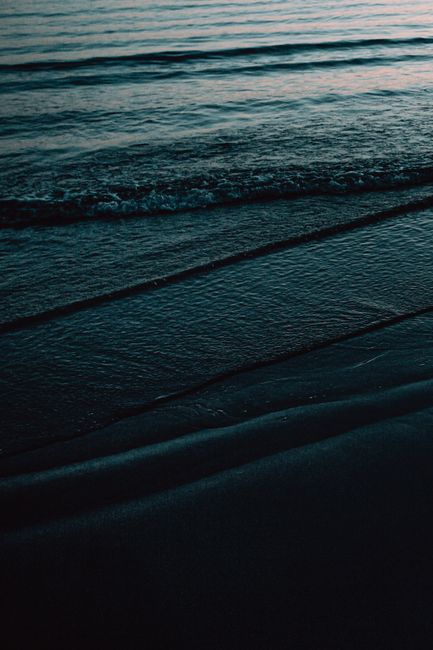A serene view of ocean waves gently reaching a dark sandy beach at dusk, capturing nature's tranquility.