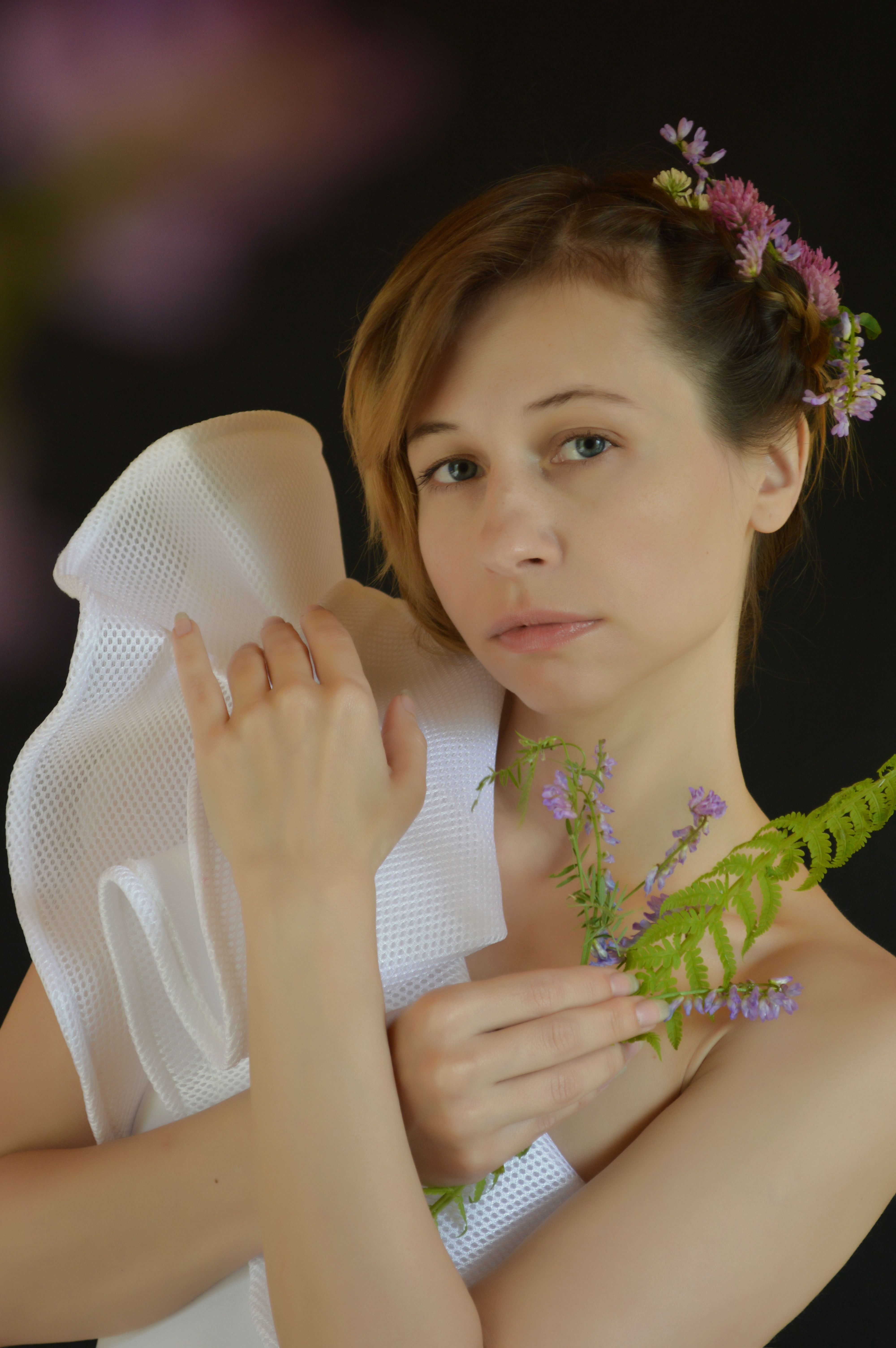 A serene woman holding flowers and fern leaves, embodying elegance and nature.