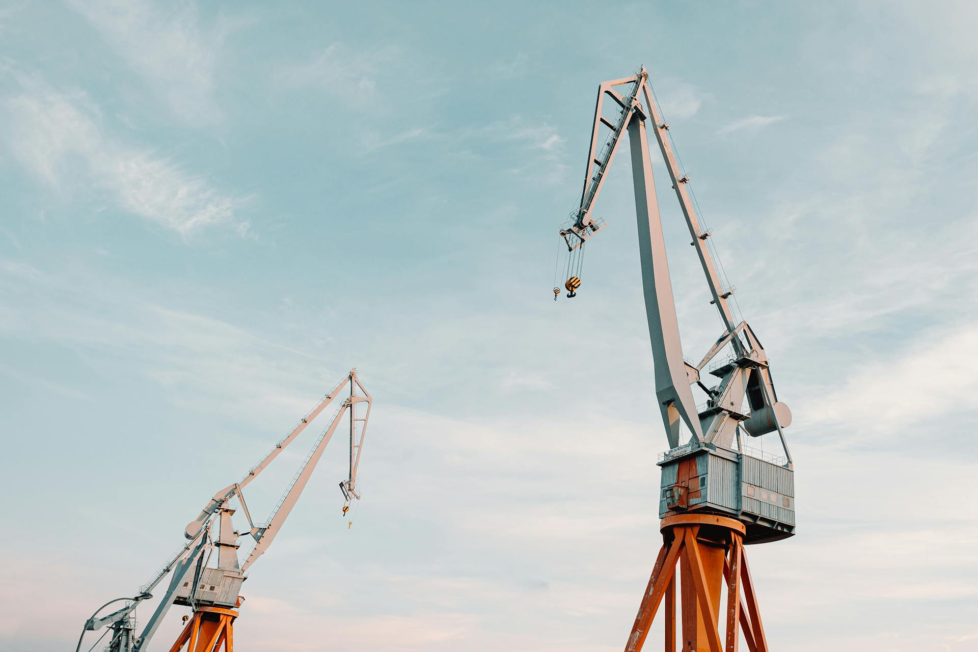 From below of metal industrial construction cranes located under clear blue sky on daytime