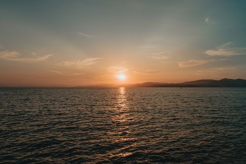 Free A tranquil ocean sunset casting warm hues across calm waters and distant hills. Stock Photo