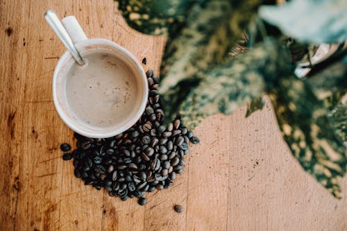 Free From above of cup of hot coffee with spoon and brown coffee beans placing on wooden table Stock Photo