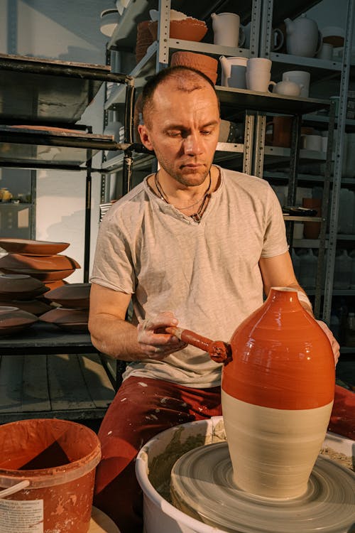 Photo of Man Painting Clay Jar With Color Brown