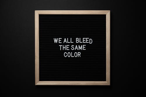 Top view of black signboard with phrase We All Bleed Same Color on surface on black background
