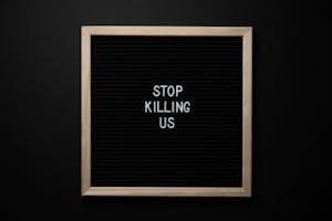 Top view of slogan Stop Killing Us on surface of square blackboard on black background
