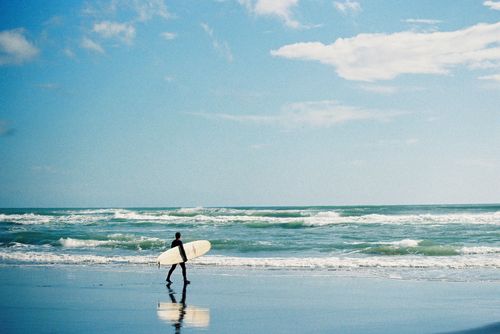 Free A lone surfer walks along Paraparaumu Beach in New Zealand, embracing the waves and summer vibe. Stock Photo