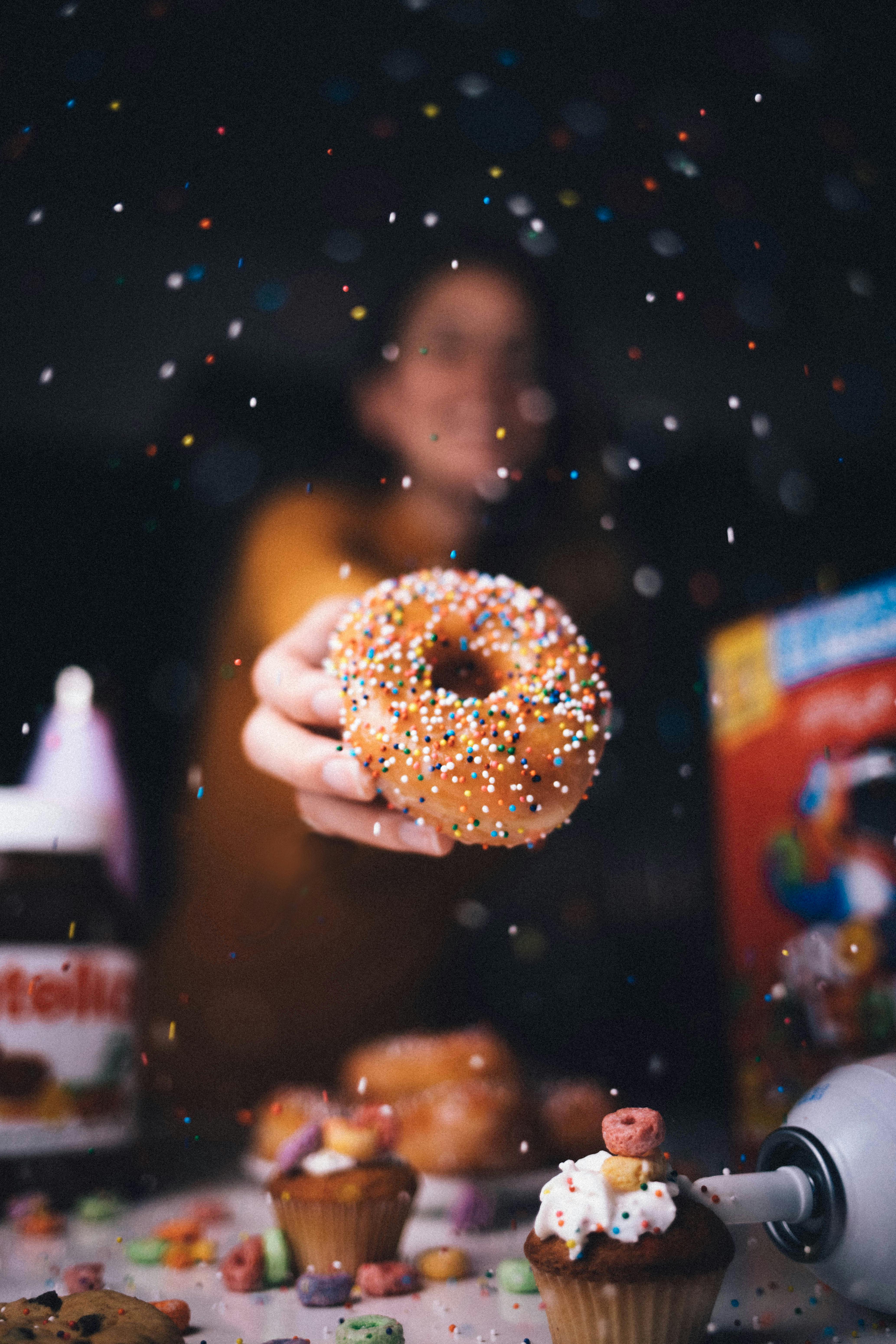 A person holding a donut with vibrant sprinkles in a creative culinary setting.