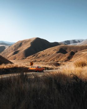 A retro car navigates a winding road in New Zealand's picturesque mountains under a clear blue sky.
