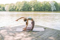 在树木环绕的湖边码头上，一位白人妇女正在表演瑜伽姿势