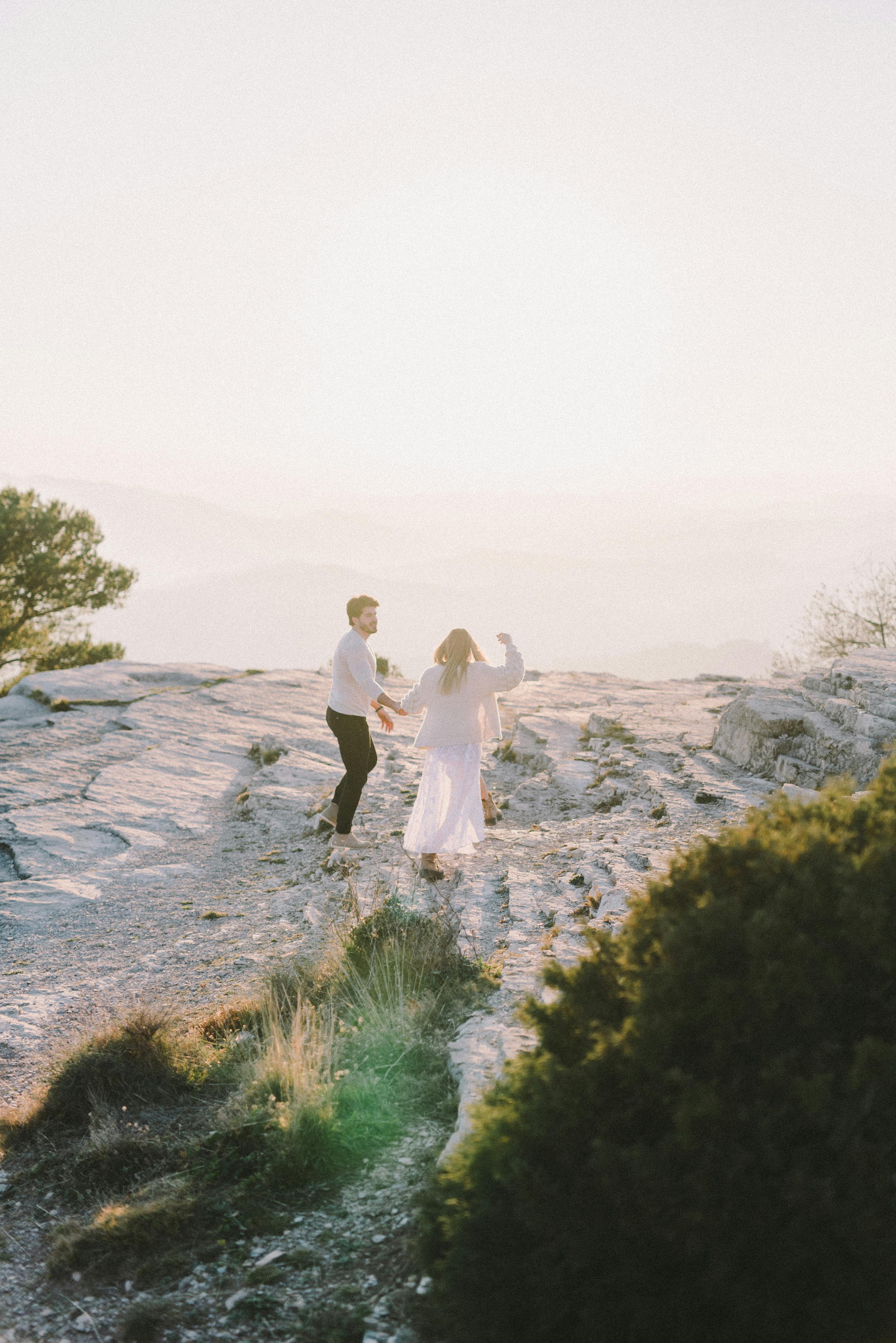 日落时分，一对夫妇手牵着手，快乐地走在崎岖的山路上