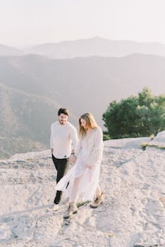 A happy couple walks hand in hand on a mountain trail, enjoying a sunny day outdoors.