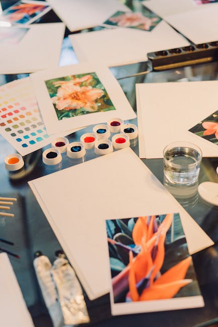 Artistic watercolor painting setup featuring vibrant paints and floral inspirations on a glass table.