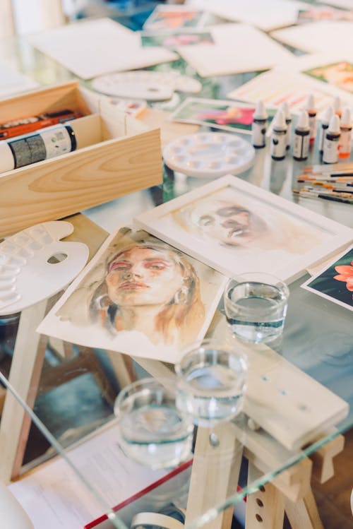 Drawn Portraits Among Art Supplies on a Glass Table