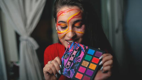 Smiling woman with colorful makeup showing eyeshadow palette