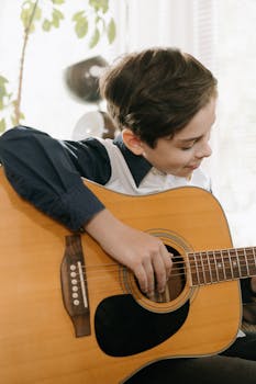 A young boy playing an acoustic guitar indoors, focused on his musical hobby.