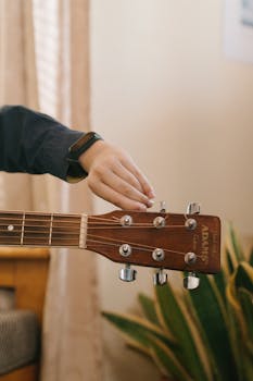 An anonymous person adjusts tuning pegs on an acoustic guitar's headstock.
