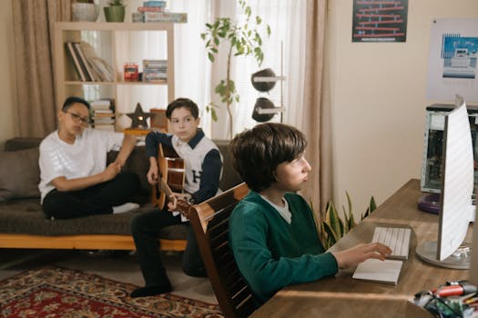 Three teenagers at home with a guitar and computer, engaged in music and tech activities.
