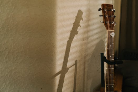 An acoustic guitar's shadow dances on a wall, creating a serene musical ambiance indoors.