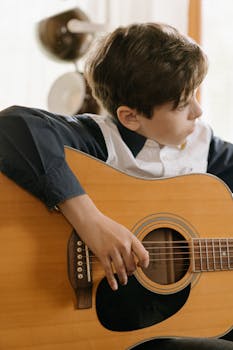 Child playing acoustic guitar indoors, focused on music and skill development.