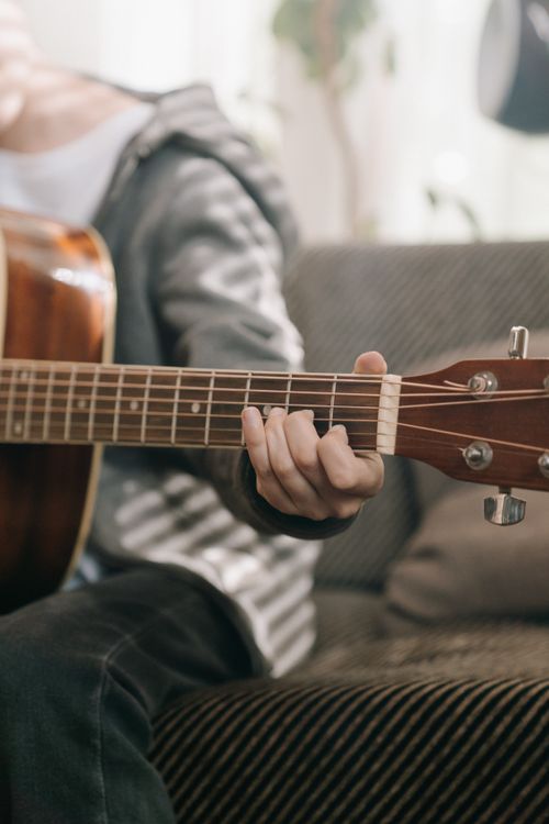 Free A person strums an acoustic guitar indoors, capturing a moment of musical creativity. Stock Photo