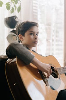 A young boy playing an acoustic guitar indoors, exuding talent and focus.
