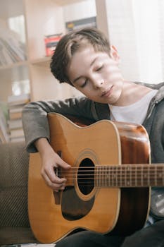 A young boy plays an acoustic guitar indoors, enjoying music and leisure time.