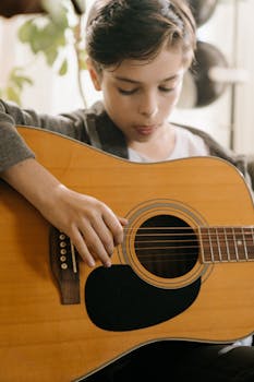 A child engages in music, strumming an acoustic guitar with focus and passion.