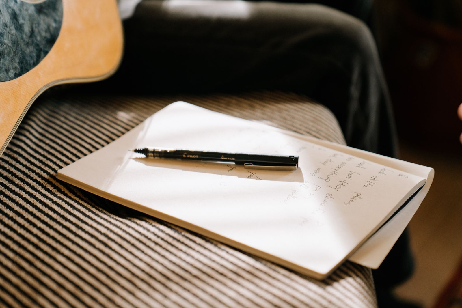 Notebook and pen resting on a couch beside an acoustic guitar