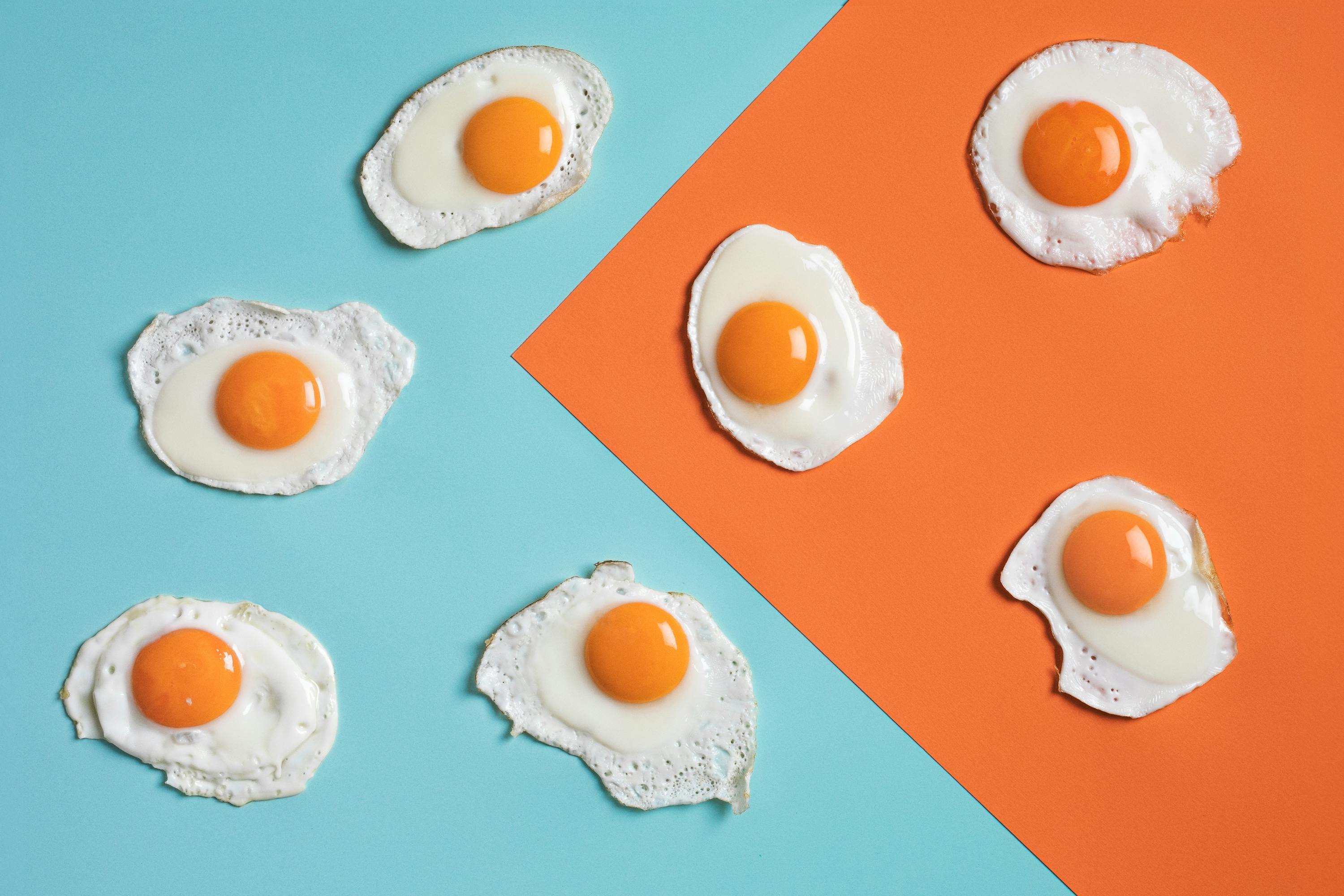 Artistic arrangement of fried eggs on vibrant blue and orange background for culinary creativity.