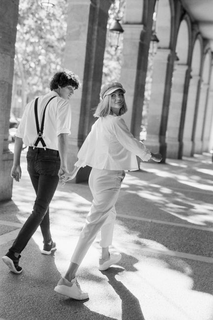 Fashionable couple walking hand in hand under archways, in black and white.