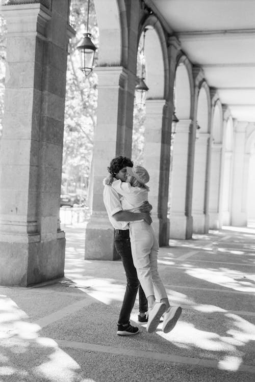 Photo En Niveaux De Gris D'un Couple S'embrassant Près D'un Bâtiment En Béton