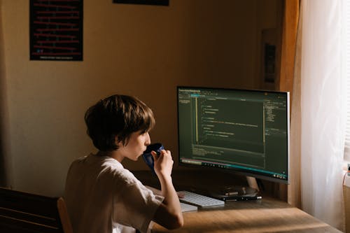 Boy in White T-shirt Sitting on Chair in Front of Computer