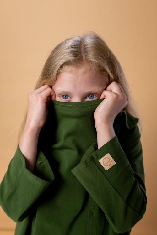 Женщина в зеленой рубашке с длинным рукавом на пуговицах закрывает лицо зеленой тканью
