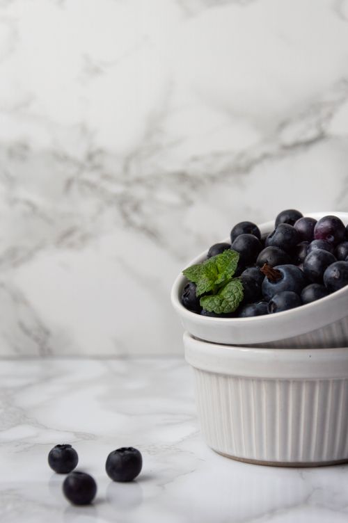 Free Fresh blueberries in a white ceramic ramekin with mint leaves on a marble surface for a clean, organic look. Stock Photo