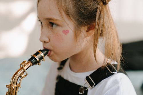 Free A young girl with heart face paint plays the saxophone indoors, exuding youthful creativity. Stock Photo