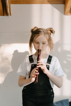 A young girl concentrating while playing a wooden recorder indoors with natural light.
