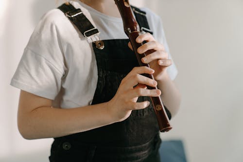 Person in White Button Up Shirt and Black Denim Jeans Holding Brown Wooden Flute
